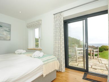 A bedroom with a bed and rolled towels next to a sliding glass door opening to an outdoor seating area at Pendower Cottage in Porthgwarra