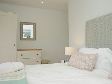 A bedroom with a bed a patterned headboard a pillow a chest of drawers a lamp and a wall mirror at Pendower Cottage in Porthgwarra