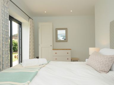 A bedroom with a bed a chest of drawers a wardrobe and glass doors with curtains at Pendower Cottage in Porthgwarra
