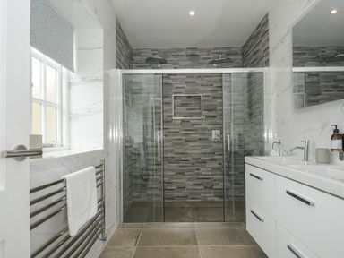 A bathroom with a double sink vanity a glass enclosed shower with dual shower heads and a towel rack at Pendower Cottage in Porthgwarra