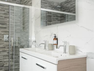A bathroom with a double sink vanity and a glass shower enclosure with gray tile walls at Pendower Cottage in Porthgwarra