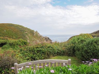 A garden bench with flowers overlooking greenery hills and the sea at Pendower Cottage in Porthgwarra