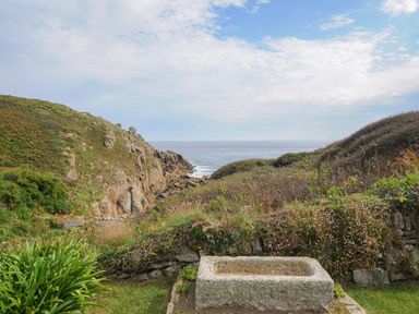 A coastal landscape with rocky hills shrubs and a stone trough at Pendower Cottage in Porthgwarra