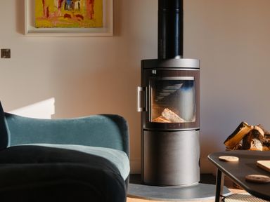 A room with a wood burning stove logs on the floor a blue sofa and a table with coasters Pendower Cottage Porthgwarra