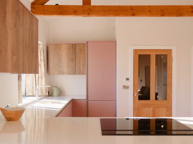 A kitchen with wooden beams wooden cabinets pink cupboards a sink kettle wooden bowl and glass panel door at Pendower Cottage in Porthgwarra