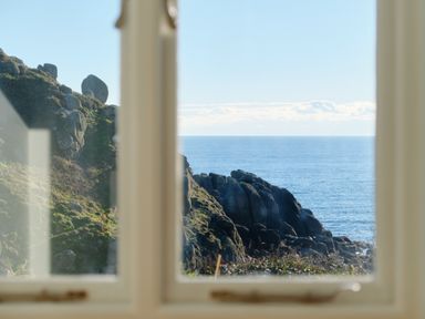 A window view of rocky cliffs and the ocean at Pendower Cottage in Porthgwarra