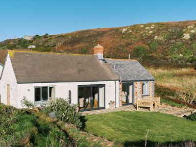 A cottage with white and brick walls with a lawn and outdoor wooden furniture at Pendower Cottage in Porthgwarra