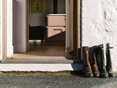 An open door showing a pink cabinet inside and two pairs of boots outside on the ground at Pendower Cottage in Porthgwarra