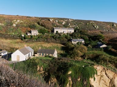 A hillside with several stone houses and vegetation at Pendower Cottage in Porthgwarra