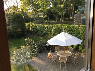 A garden with a round wooden table and chairs under a white umbrella and shrubs and trees at Gull Rock 4 Rock