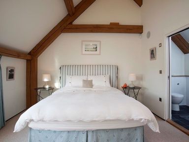 A bedroom with a large bed with striped headboard two bedside tables with lamps and an open door showing a bathroom at Gull Rock 4 in Rock