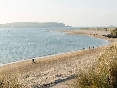 A sandy beach with people walking near the water and grassy dunes at Gull Rock 4 in Rock
