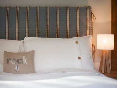 A bed with a striped headboard a white pillow with buttons a small pillow with the word rock and a lamp on a bedside table at Gull Rock 4 in Rock