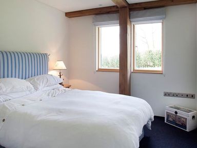 A bedroom with a bed with striped headboard two windows and a lamp on a bedside table at Gull Rock 4 in Rock