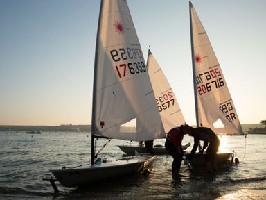 Two people preparing small sailboats on the water at sunset at Gull Rock 4 in Rock
