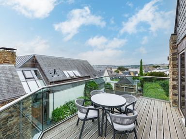 A balcony with glass railing and a round table with four chairs overlooking neighboring rooftops and greenery at Gull Rock 4 in Rock