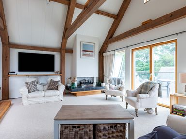 A living room with wooden beams television fireplace armchairs and large windows at Gull Rock 4 Rock