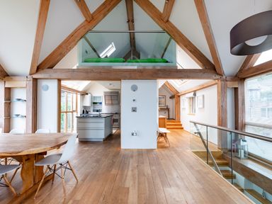 An open plan room with wooden beams a dining table white chairs a kitchen area and a staircase with glass railing at Gull Rock 4 in Rock