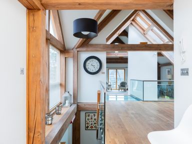 A modern loft space with wooden beams a large clock and two armchairs by a window at Gull Rock 4 in Rock