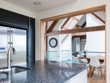 A kitchen with a granite countertop sink and stainless steel refrigerator opening to a dining area with a wooden table white chairs and a wall clock at Gull Rock 4 in Rock
