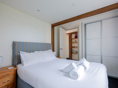 A bedroom with a bed with a striped headboard and folded towels on top next to wooden bedside tables with lamps and a sliding door wardrobe at Gull Rock 4 in Rock