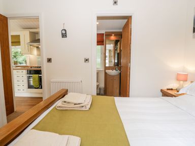 A bedroom with a bed towels bedside table and lamp with doors leading to a kitchen and bathroom at Pippin Lodge in Allithwaite near Cartmel