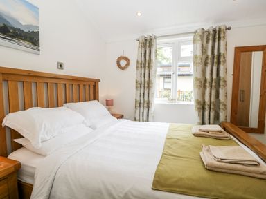 A bedroom with a double bed wooden furniture window with curtains and folded towels at Pippin Lodge in Allithwaite near Cartmel