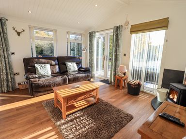 A living room with a brown leather sofa a wooden coffee table a rug and a wood stove at Pippin Lodge in Allithwaite near Cartmel
