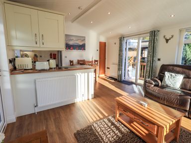 A living room with a brown leather sofa a wooden coffee table and a dining table near the kitchen at Pippin Lodge in Allithwaite near Cartmel