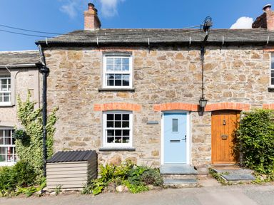 Stone cottage with blue and wooden doors and two windows with plants outside at Stokes Cottage in St Minver