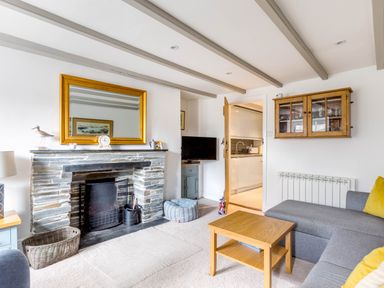 A living room with a stone fireplace a wooden coffee table a gray sofa with yellow pillows and a wall cabinet at Stokes Cottage in St Minver