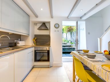 A kitchen with white cabinets oven and dining table with yellow chairs at Stokes Cottage in St Minver