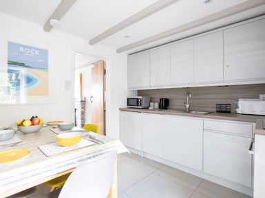 A kitchen with white cabinets a dining table set with bowls and plates and a fruit bowl at Stokes Cottage in St Minver