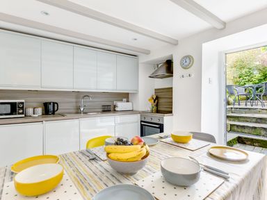 A kitchen with white cabinets a dining table set with bowls plates and fruit at Stokes Cottage in St Minver