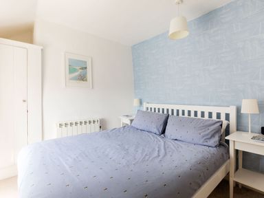 A bedroom with a double bed with blue bedding and two side tables with lamps at Stokes Cottage in St Minver