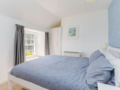 A bedroom with a bed covered in blue bedding next to a window with grey curtains at Stokes Cottage in St Minver