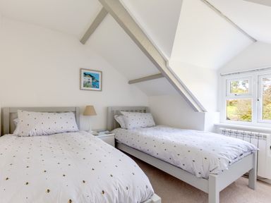 A bedroom with two single beds a bedside table and a window at Stokes Cottage in St Minver