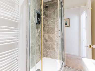 A bathroom with a glass shower enclosure tiled walls and a white towel radiator at Stokes Cottage in St Minver