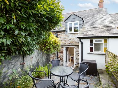 A small patio with a round glass table and four chairs next to a stone and white cottage at Stokes Cottage in St Minver