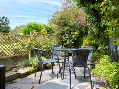 A patio area with four chairs and a round table surrounded by plants at Stokes Cottage in St Minver