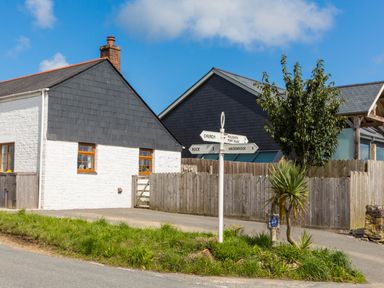 A street corner with directional signs near houses with a wooden fence and trees at Stokes Cottage in St Minver