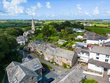 An aerial view of a village with stone and white houses a church with a tall steeple and green fields at Stokes Cottage in St Minver