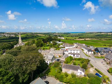 A village with houses trees and fields under a blue sky at Stokes Cottage in St Minver