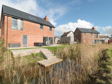 Two brick houses with black roofs near a water body with wooden steps and tall grass at Agua de Plata 16 Wakeling Island Silverlake in Dorchester