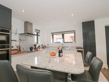 A kitchen with a marble countertop island with bottles and glasses and black chairs at Agua de Plata 16 Wakeling Island Silverlake in Dorchester