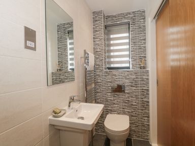A bathroom with a sink mirror toilet vertical striped tiles and a wooden sliding door at Agua de Plata 16 Wakeling Island Silverlake in Dorchester
