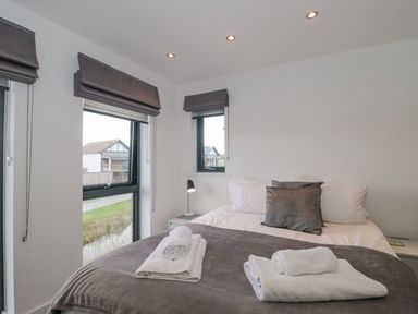 A bedroom with a bed and folded towels on a blanket next to two windows with gray blinds at Agua de Plata 16 Wakeling Island Silverlake in Dorchester