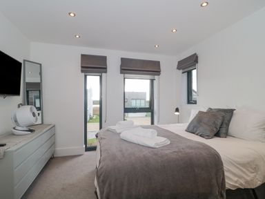 A bedroom with a bed, pillows, folded towels, dresser with fan, wall mirror, mounted TV, and windows with blinds at Agua de Plata 16 Wakeling Island Silverlake in Dorchester
