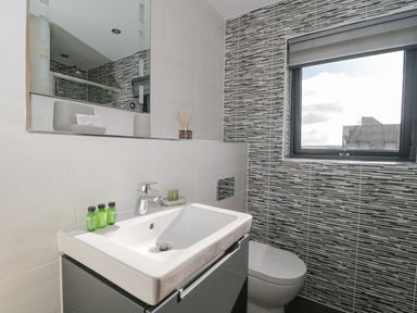 A bathroom with a sink, mirror, small bottles, and a window showing an outside building at Agua de Plata, 16 Wakeling Island, Silverlake in Dorchester