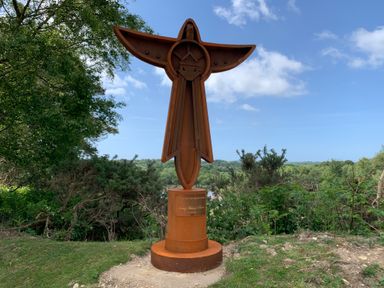 A metal cross-shaped sculpture on a round base surrounded by grass and trees at Agua de Plata 16 Wakeling Island Silverlake